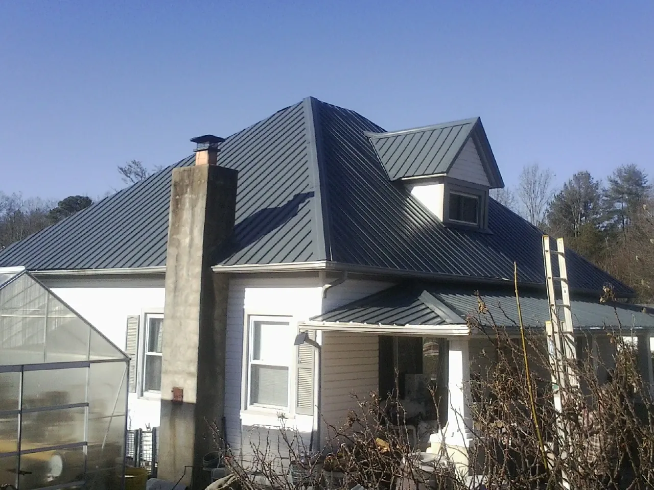 Dark blue standing seam metal roof on a white farmhouse with dormer — Slate & Tile Roof Repair by Roofing Brothers in Fort Sill