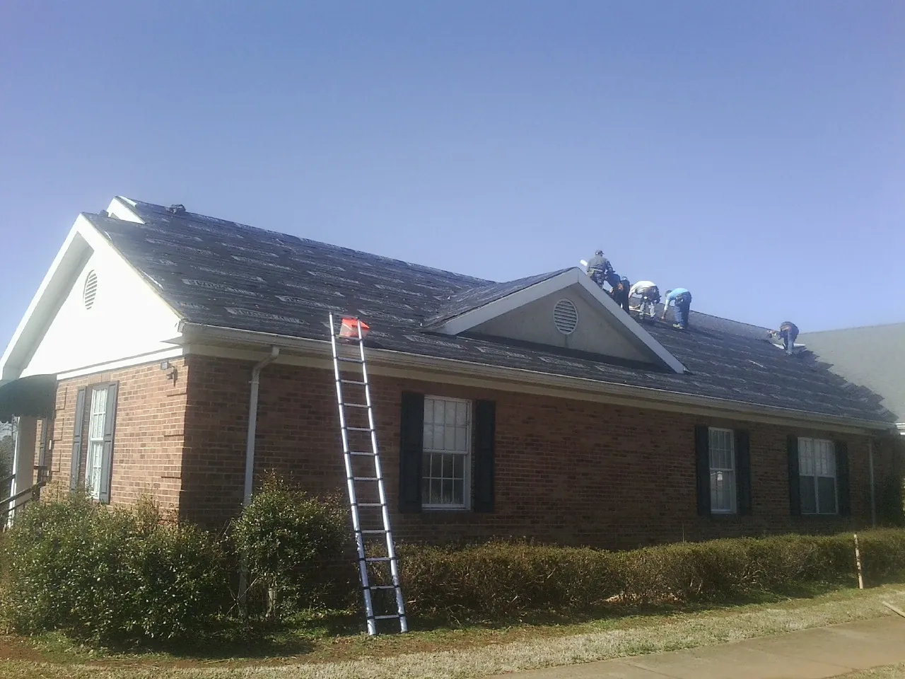 Crew tearing shingles off a brick ranch roof with a ladder set — Emergency Roof Repair work by our crew in Fort Sill