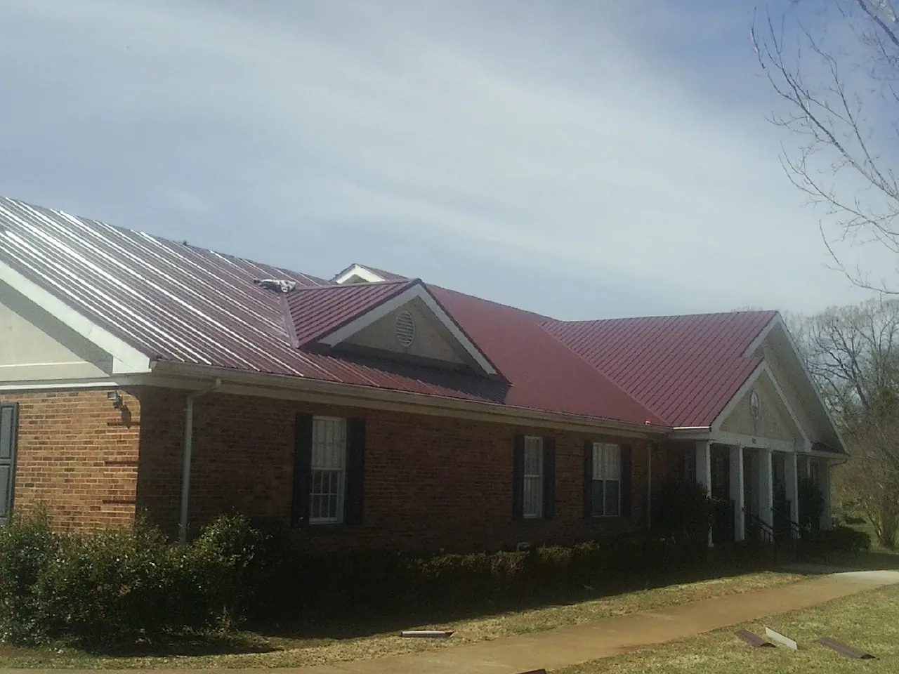 Red metal roof with gabled entries on a long brick building, from a Hail Damage Roof Repair job in Fort Sill