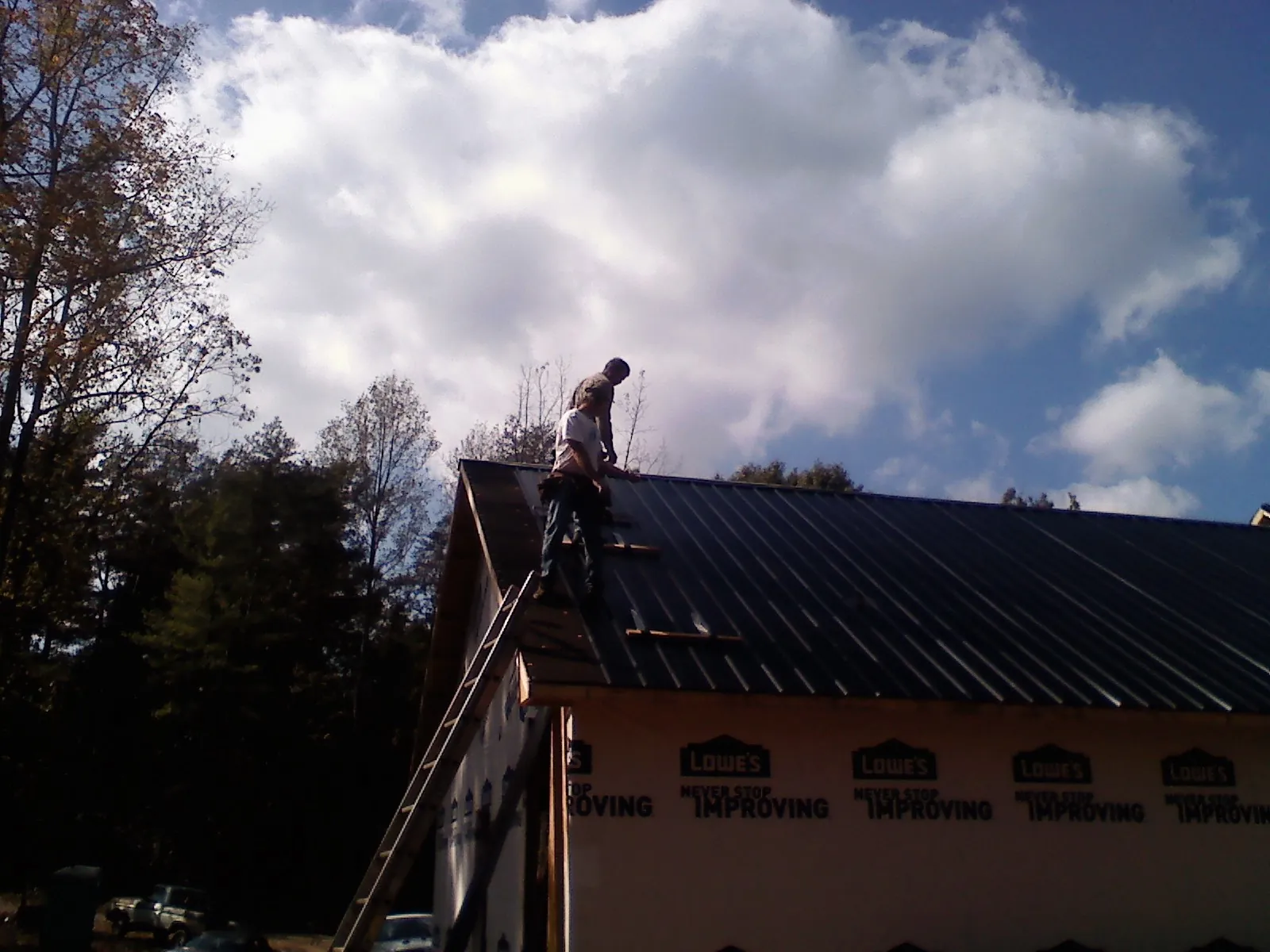 Roofer fastening dark metal panels high against a cloudy sky, from a Roof Inspection job in Fort Sill