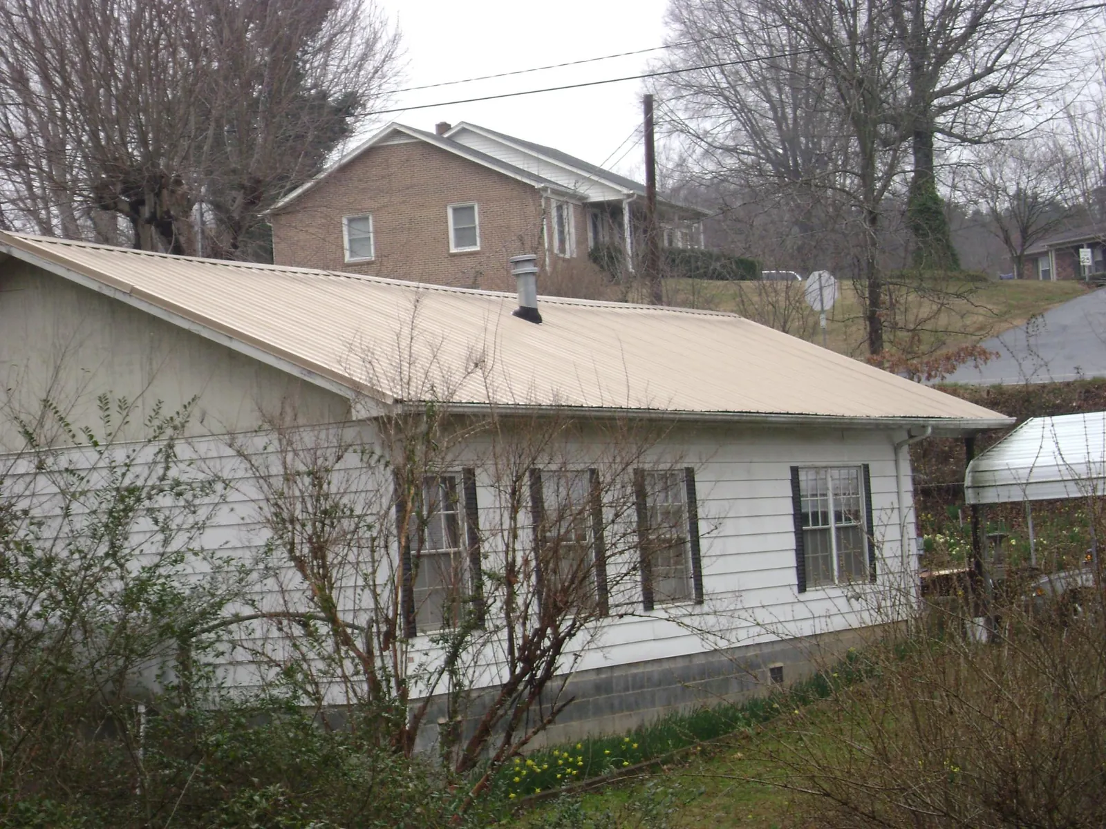 Tan metal roof on a white sided house set into a hillside — Commercial Roofing by Roofing Brothers in Fort Sill